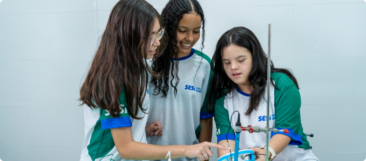 Na imagem, lê-se: três crianças, duas ao fundo desfocada e uma na frente olhando para a câmera sorrindo e fazendo gesto de joinha.