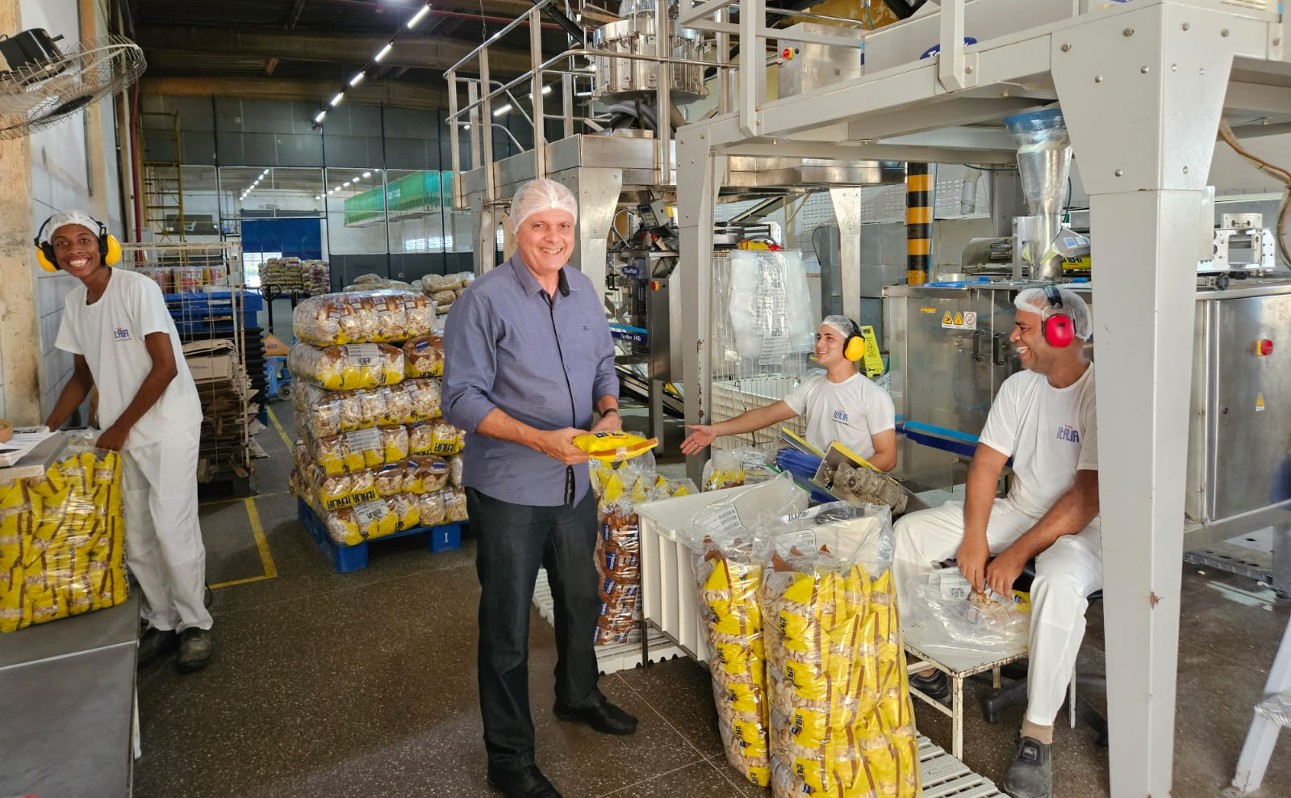 Homem sorrindo com touca segura pacote de biscoitos em fábrica