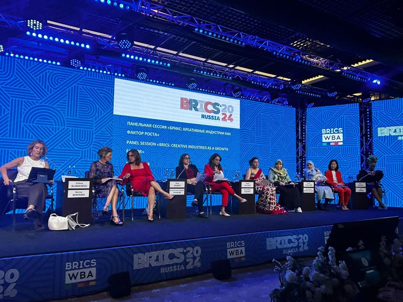 Mulheres sentadas em palco com fundo azul