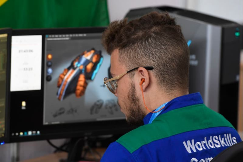Jovem branco de óculos de costas sentado em computador com a tela com desenho preto, laranja e azul