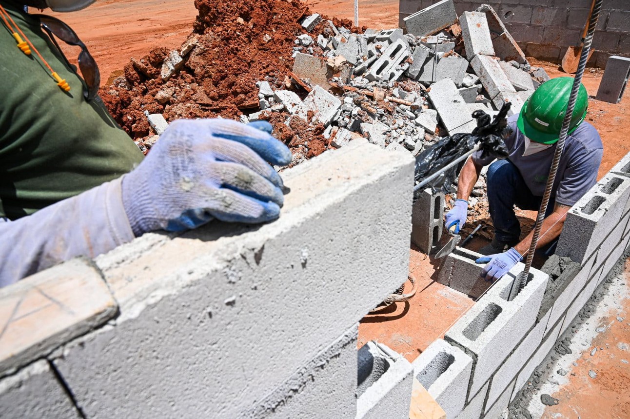 Dois homens trabalhando em construção de parede com equipamentos de segurança