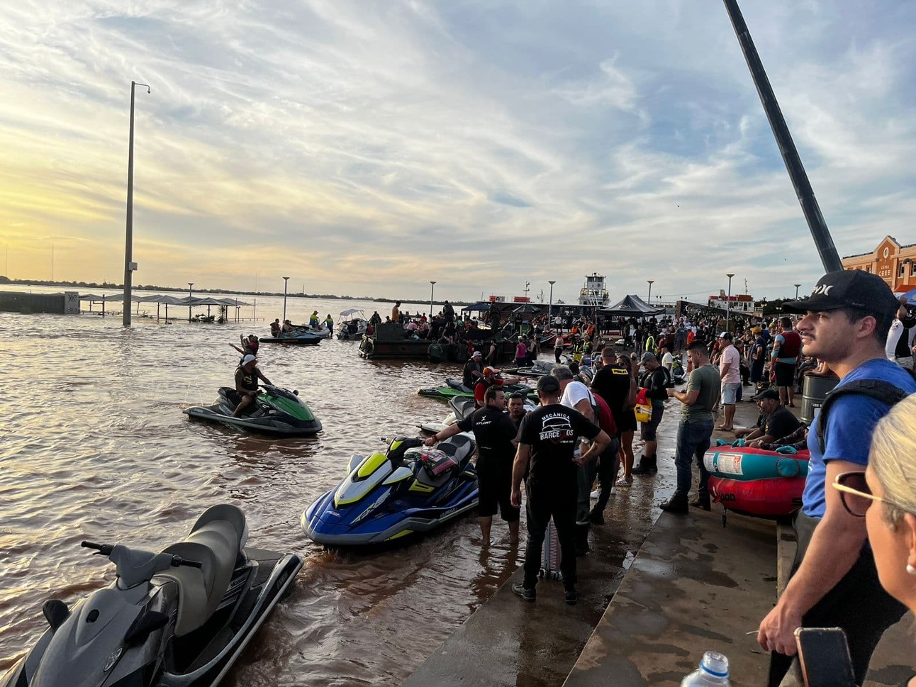 foto colorida mostra beira do rio Guaíba com jetskis na água, além de socorristas e pessoas a espera de ajuda no Rio Grande do Sul