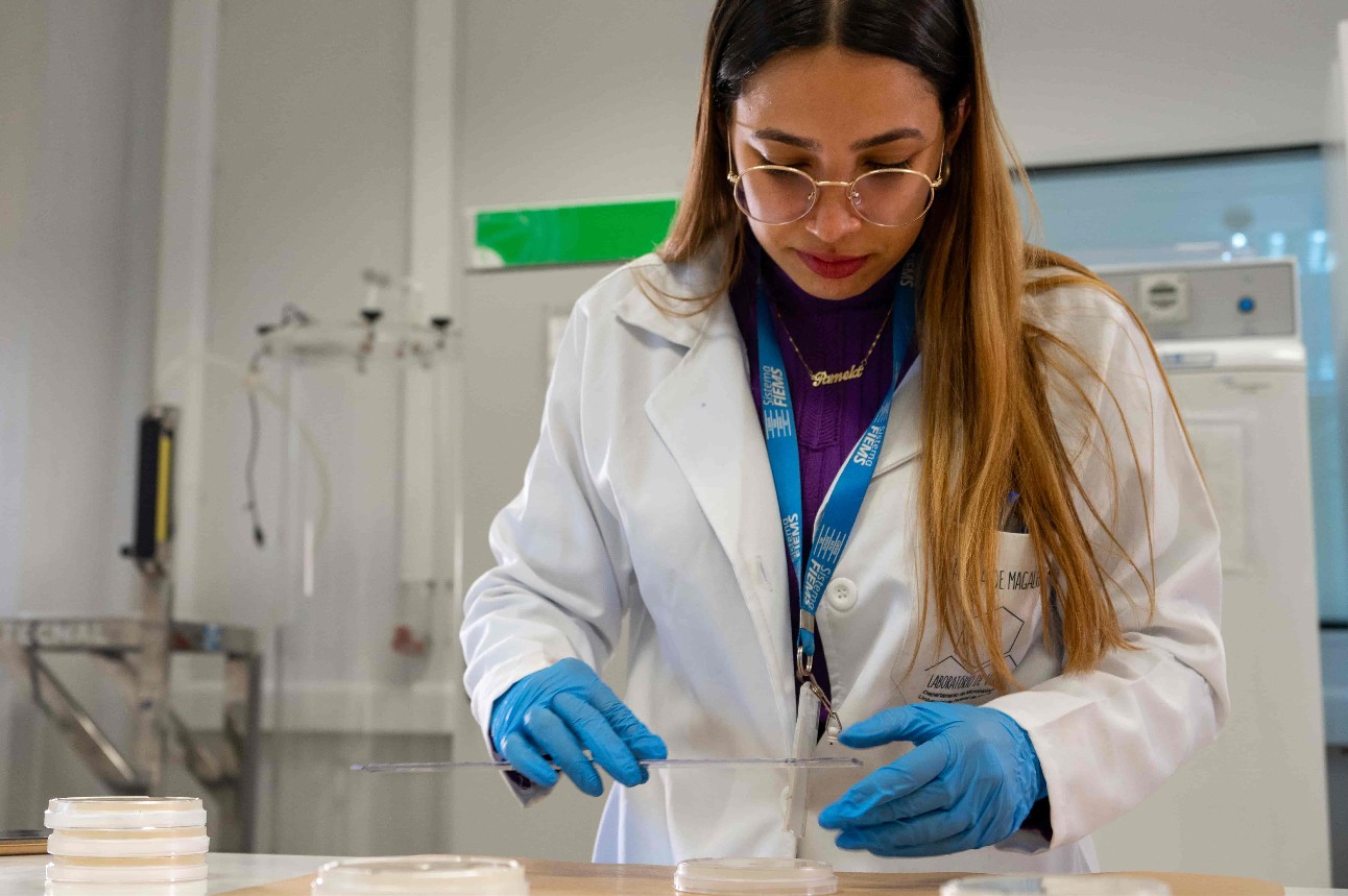 Jovem mulher fazendo experimentos em um laboratório. Ela usa óculos e crachá - veste um jaleco, luvas.