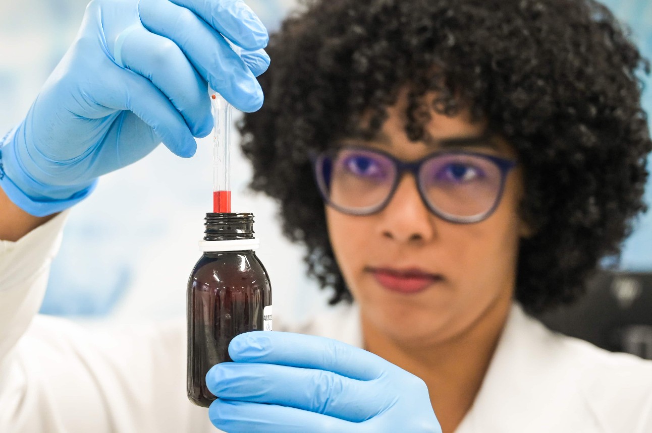 Mulher negra usando luvas azuis trabalha com tubo de ensaio e frasco de vidro em laboratório