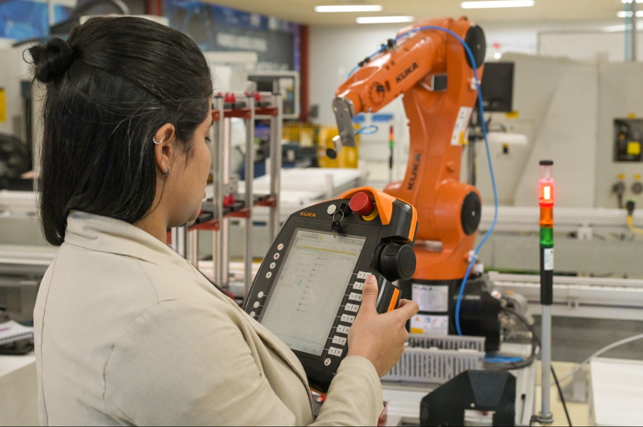 Mulher com equipamento digital em frente a planta com robô