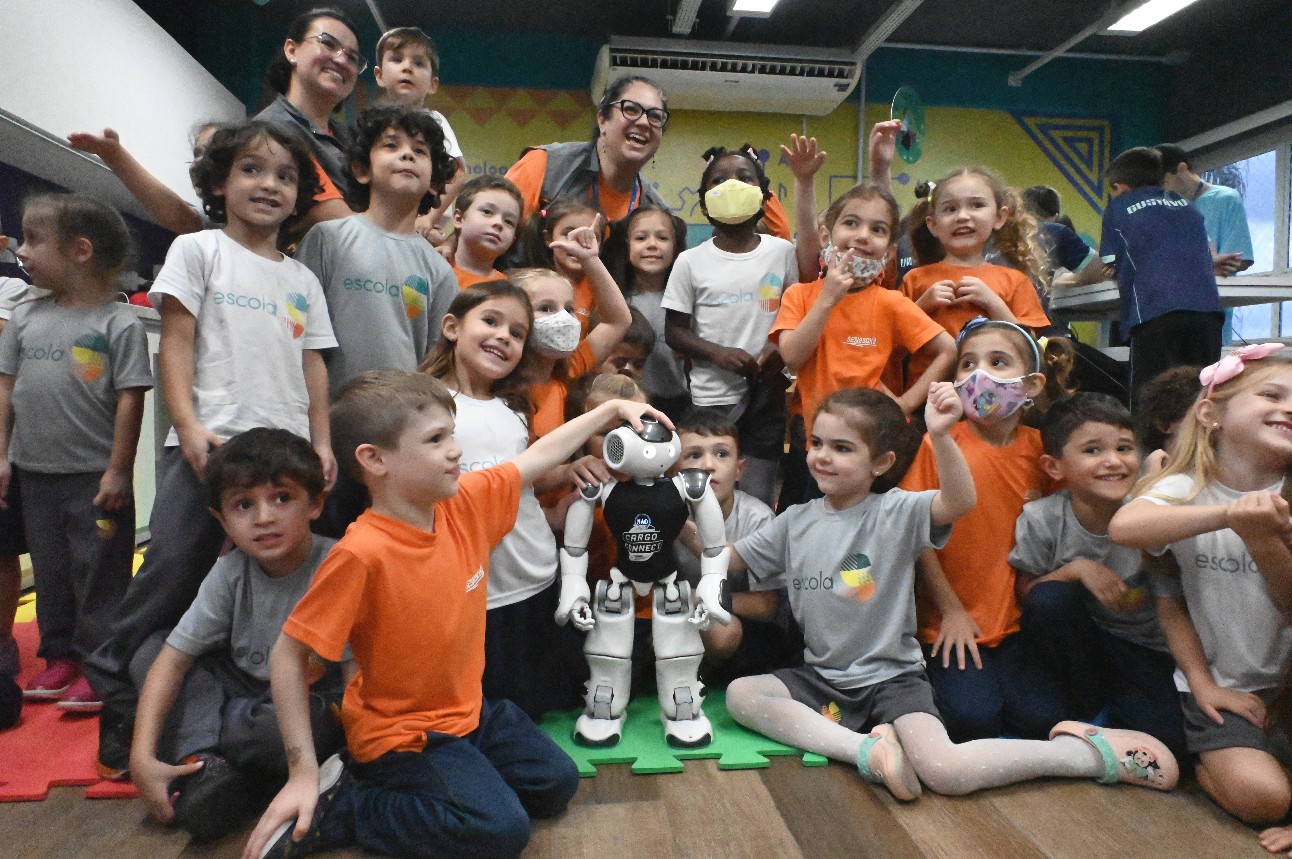 Um robô humanoide está no centro da imagem e várias crianças estão em volta dele