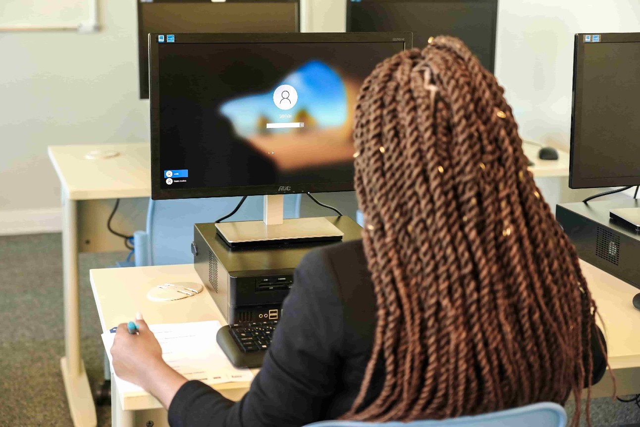 imagem colorida de mulher negra, com tranças, mexendo em computador