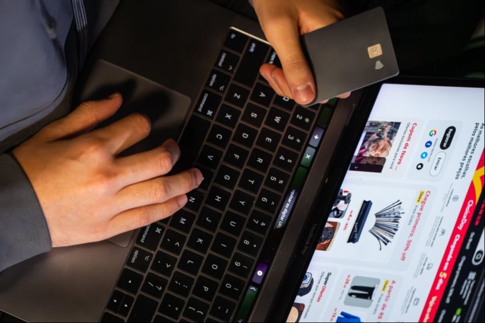 Homem faz compra on-line utilizando computador e cartão de crédito