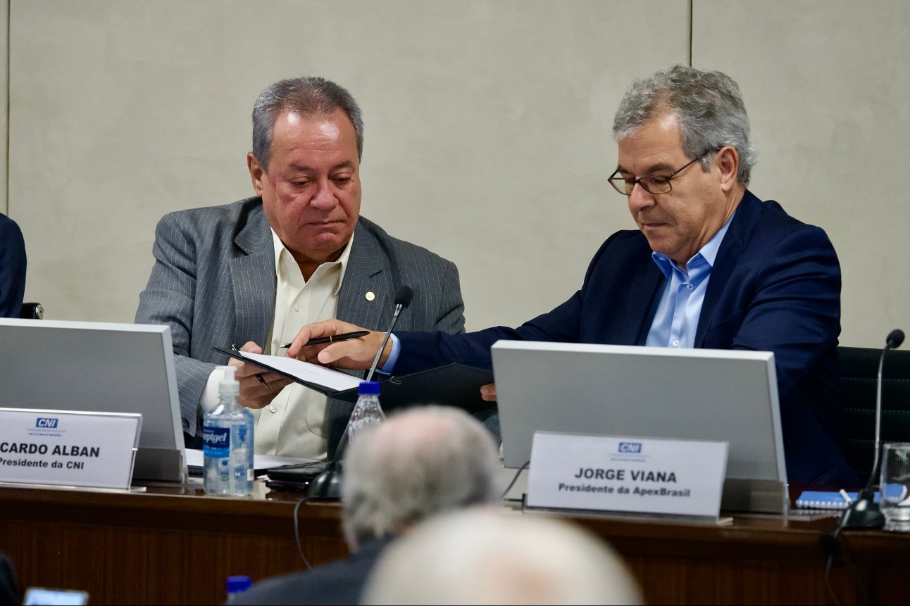 Dois homens brancos de terno sentados segurando documento