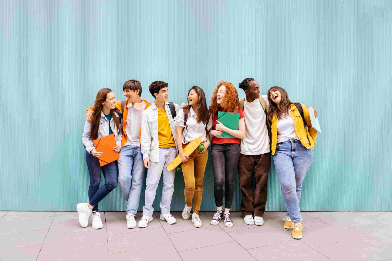 Estudantes felizes em pé sobre fundo azul isolado. Diversos amigos adolescentes se divertindo conversando apoiados na parede.