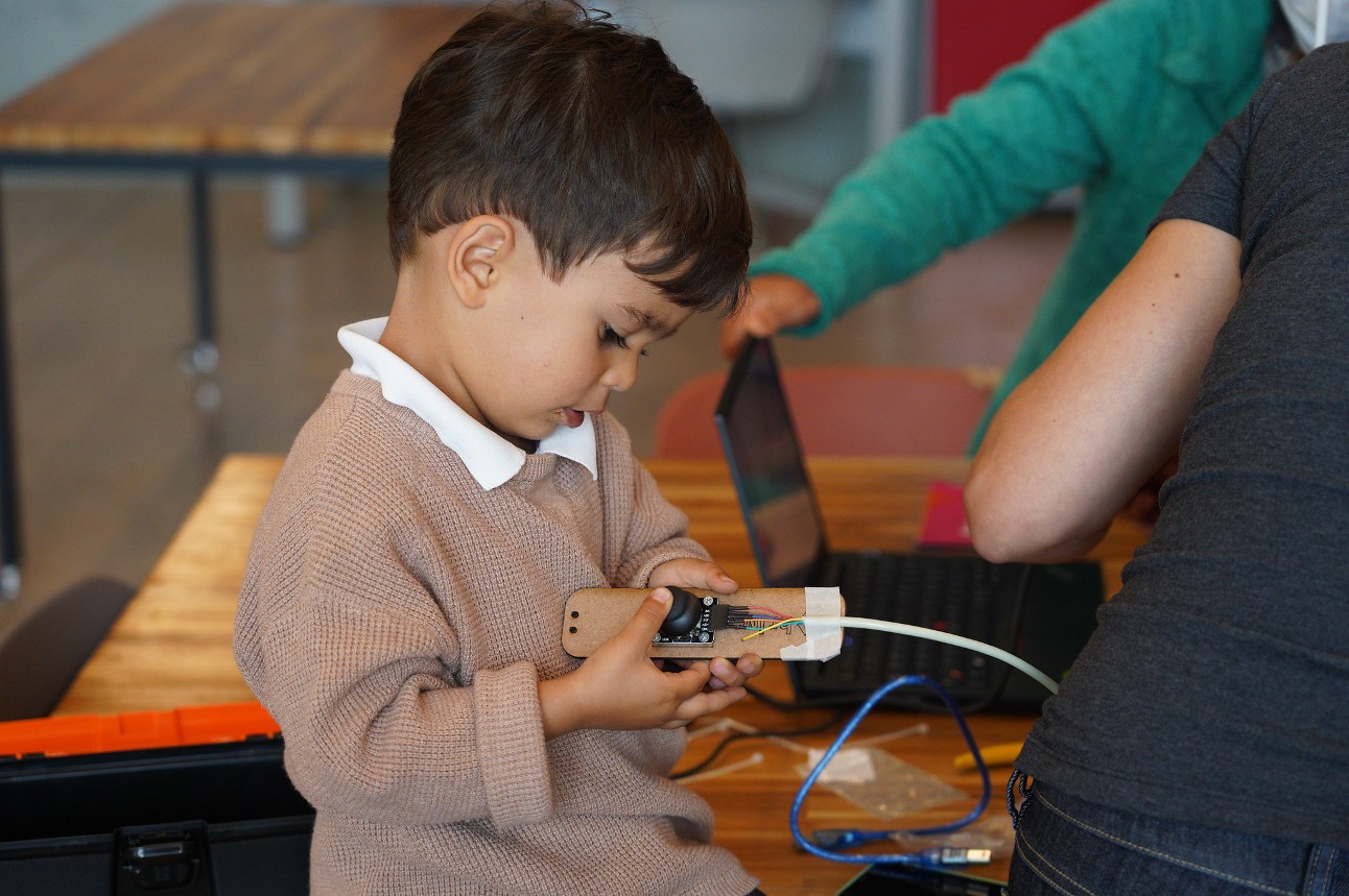 Menino de aproximadamente 4 anos olha curioso para um dispositivo eletrônico em oficina maker do SESI Lab