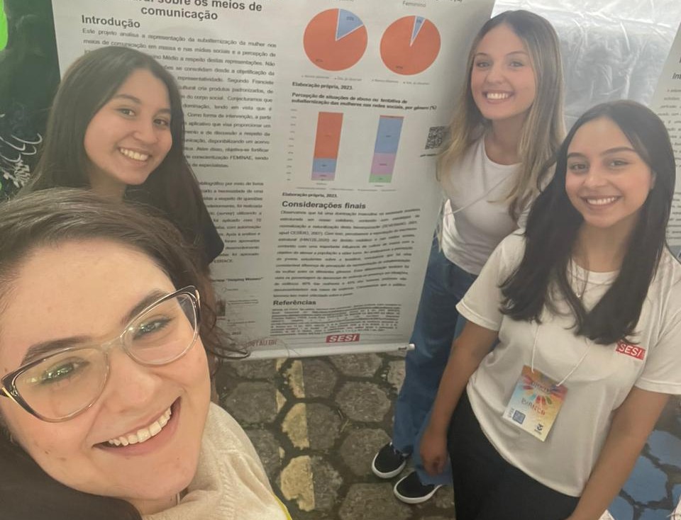 Selfie de quatro mulheres. Atrás, há um banner de iniciação científica