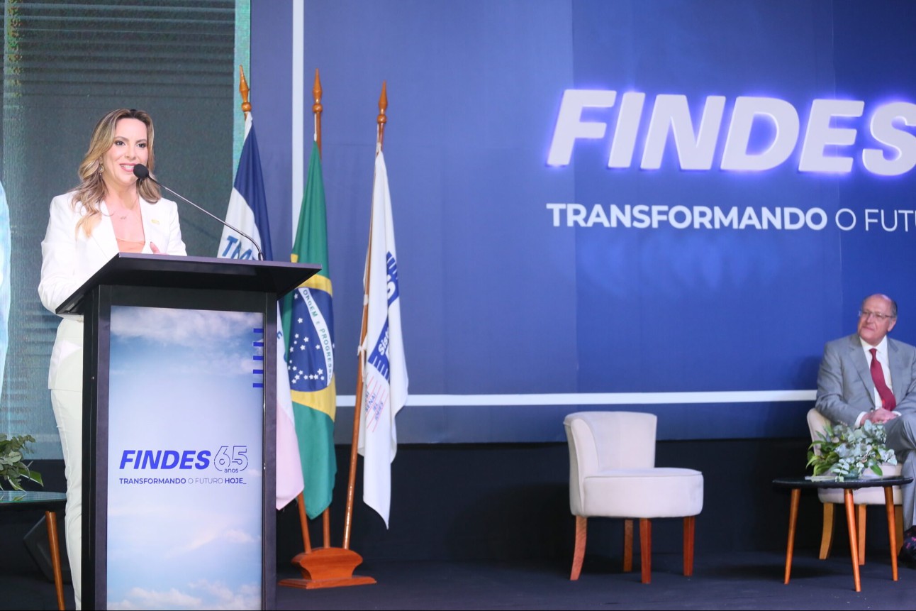 O evento comemorativo, que aconteceu no Ilha Buffet, em Vitória, reuniu industriais, empresários e representantes do setor produtivo e do Poder Público mulher branca palestrando, usa roupas brancas e tem o cabelo solta, ela está falando ao microfone e ao fundo tem um cartaz com a logo da FINDES