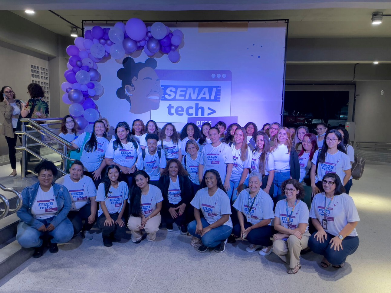 Após o sucesso do primeiro programa (foto da turma), mais mulheres poderão se qualificar para o mercado de tecnologia Grupo de mulheres posam juntas, todas usam uniforme com camiseta branca e calça.