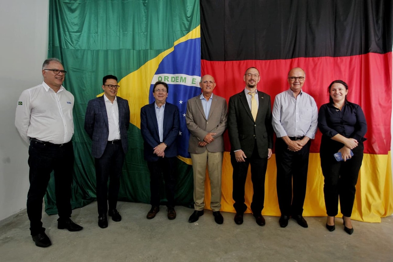 Cinco homens e uma mulher posam para foto em frente às bandeiras do Brasil e da Alemanha