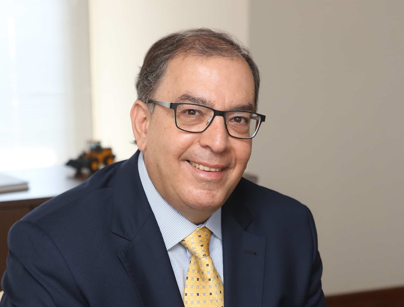 José Velloso, presidente-executivo da ABIMAQ, com óculos quadrado, terno preto e gravata amarela, posa para foto com sorriso