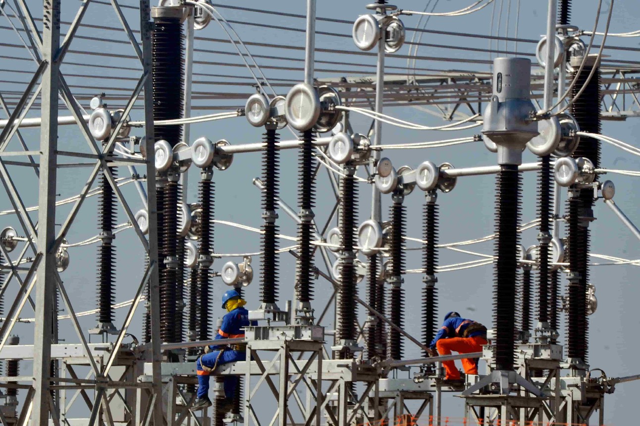 Estruturas metálicas de energia elétrica com dois trabalhadores com roupas azul e laranja