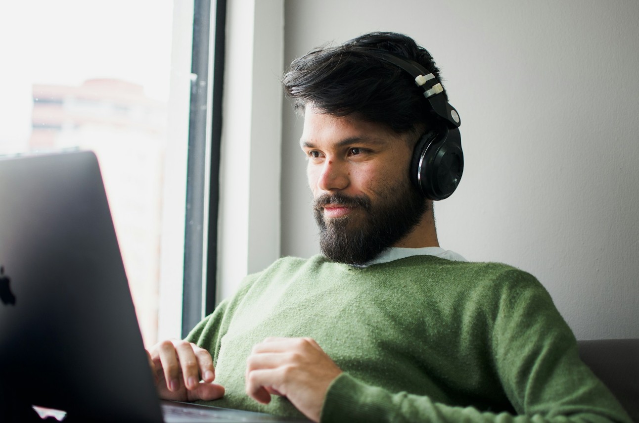 Homem olhando para seu MacBook enquanto escuta algo no seu fone de ouvido sem fio