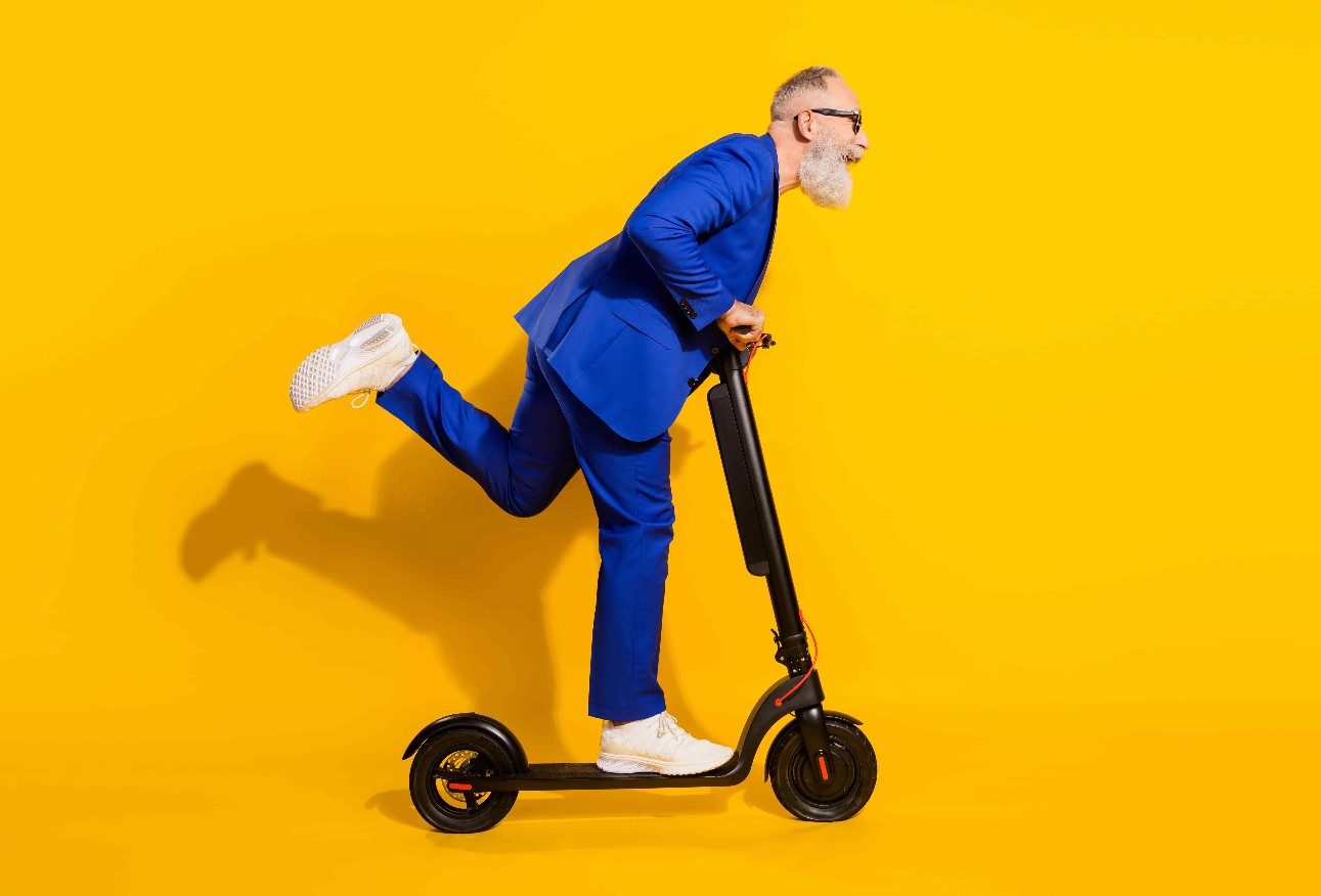 Foto do lado do perfil em tamanho real de um homem maduro, louco e feliz, parece copyspace montando uma scooter isolada em um fundo de cor amarela