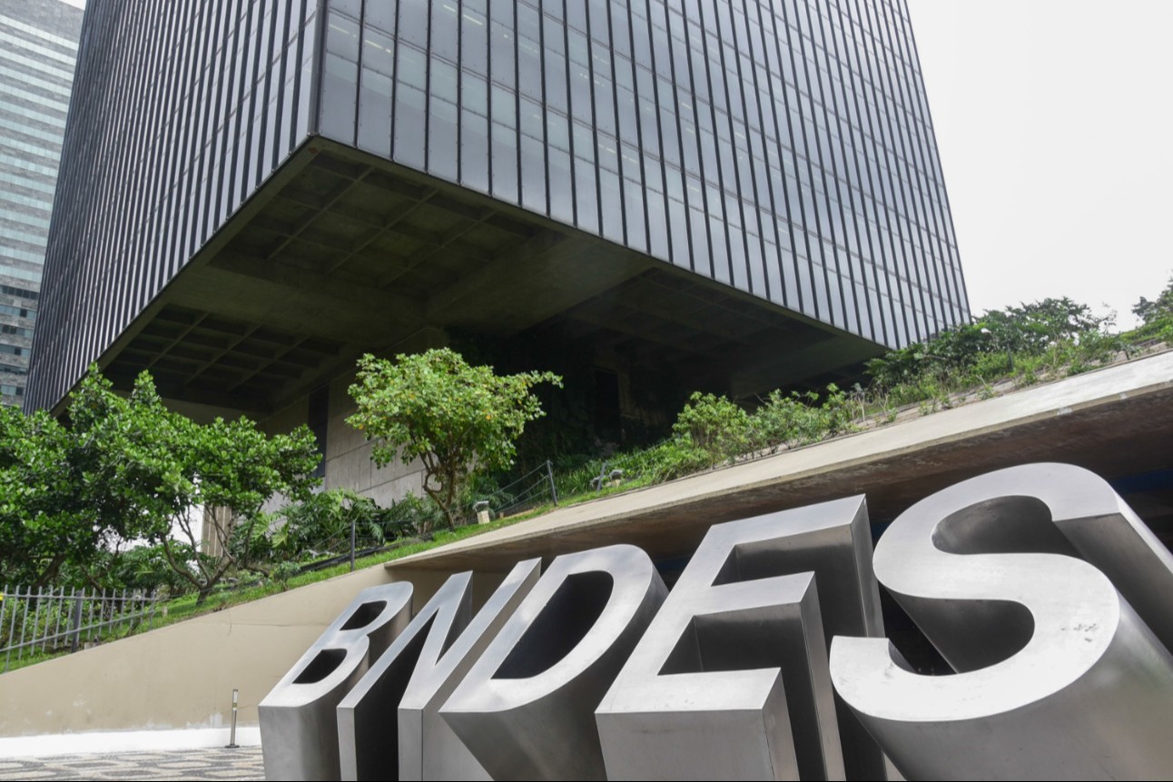 Foto colorida traz em primeiro plano letreiro de identificação da fachada da sede do BNDES