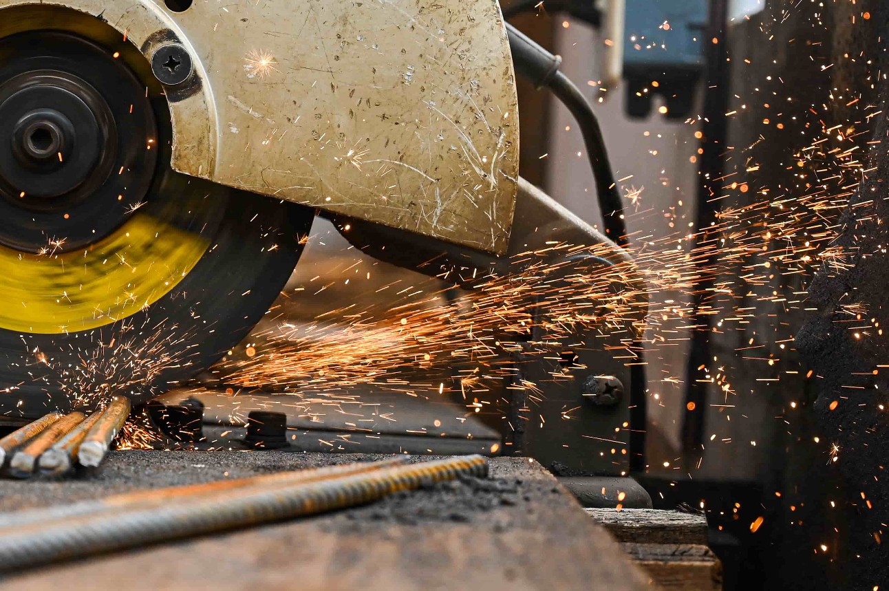 Imagem: serra industrial amarela cortando aço e soltando faíscas