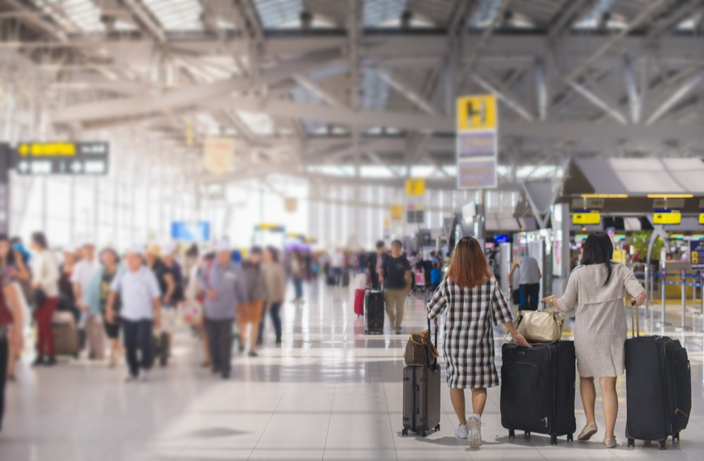 imagem colorida de espaço de aeroporto, com pessoas circulando com malas