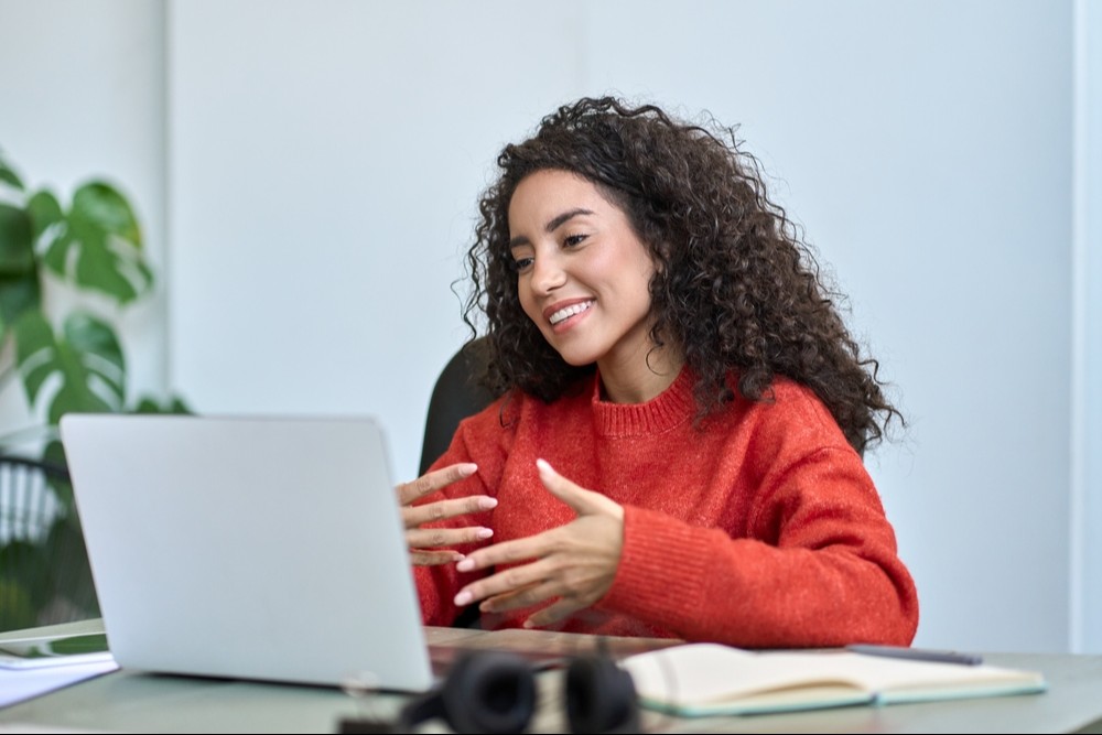 imagem colorida de mulher de cabelos cacheados vestindo suéter vermelho e gesticulando para computador