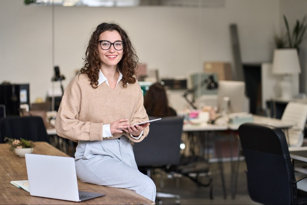 Uma linda jovem mulher de negócios profissional sorridente, gerente corporativa, funcionária segurando um tablet digital com tecnologia fintech no local de trabalho em um escritório moderno, olhando para a câmera.