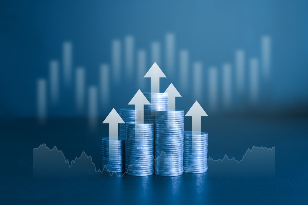 Pilha de moedas com seta branca ascendente e gráfico ao fundo. Conceito financeiro e empresarial com filtro de cor azul.