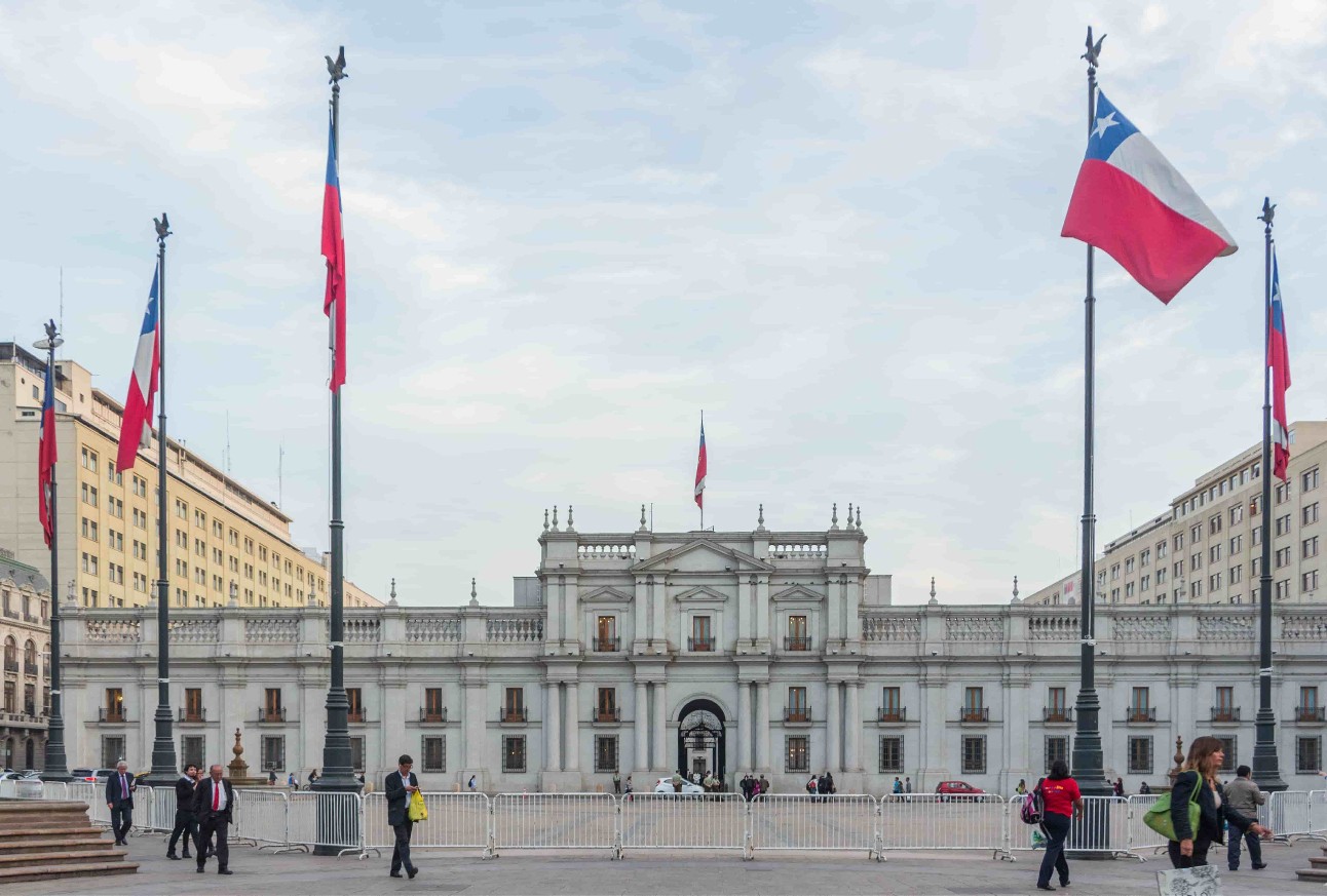 Fachada de prédio claro com bandeiras do Chile na frente e céu nublado ao fundo