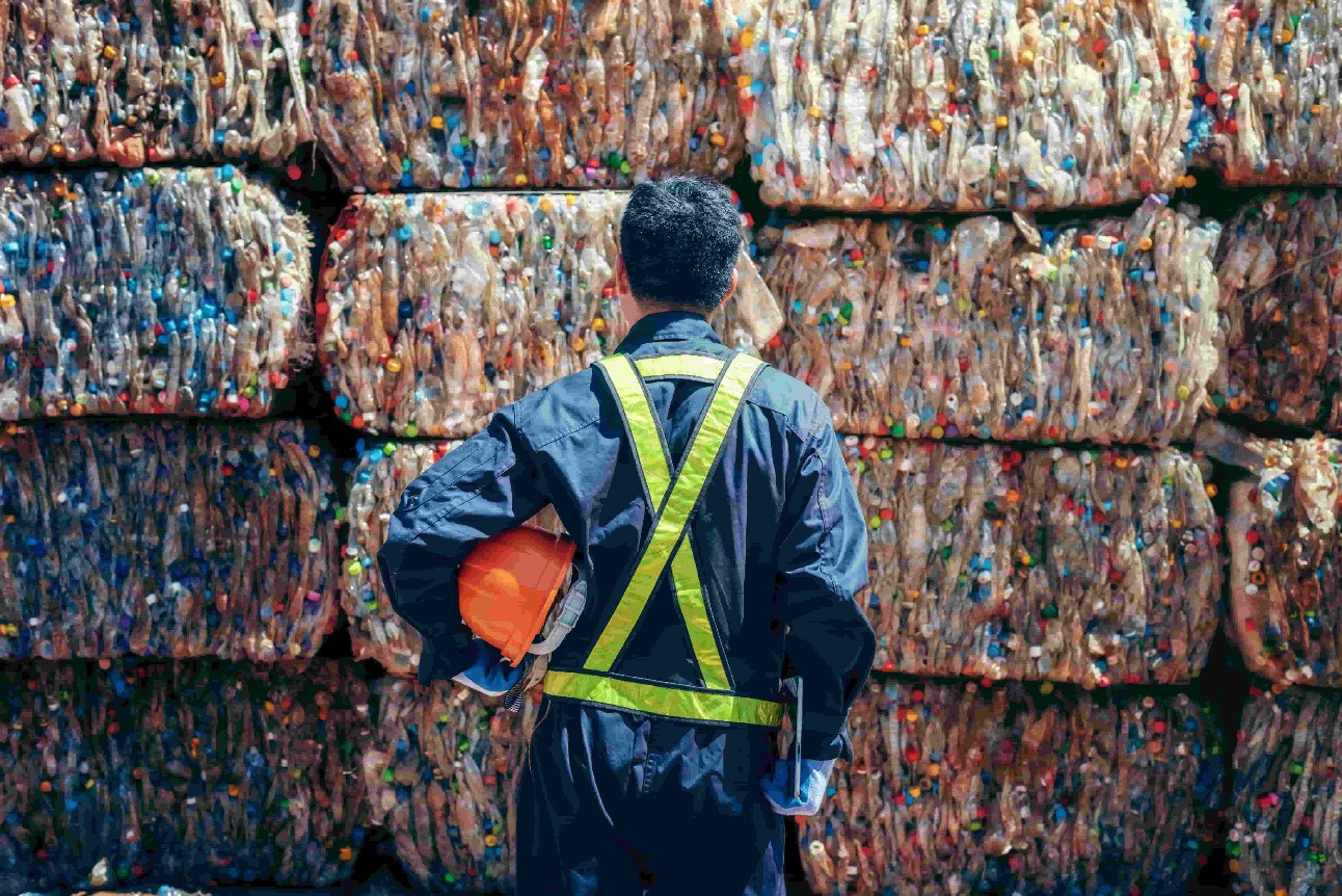 Homem com roupa de segurança de costas olhando para plásticos a serem reciclados