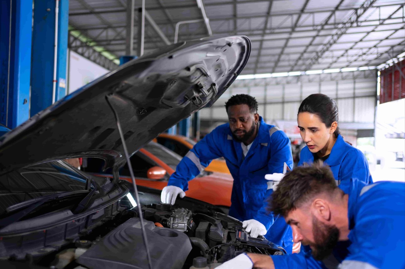 Tres pessoas, dois homens e uma mulher, mexendo na mecânica de um carro