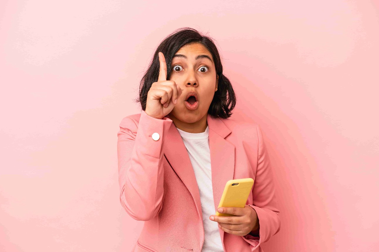 Jovem latina segurando celular em fundo rosa, tendo uma ideia, conceito de inspiração.