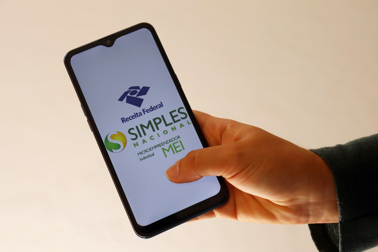 Pessoa segurando smartphone com aplicativo do Simples Nacional aparecendo na tela