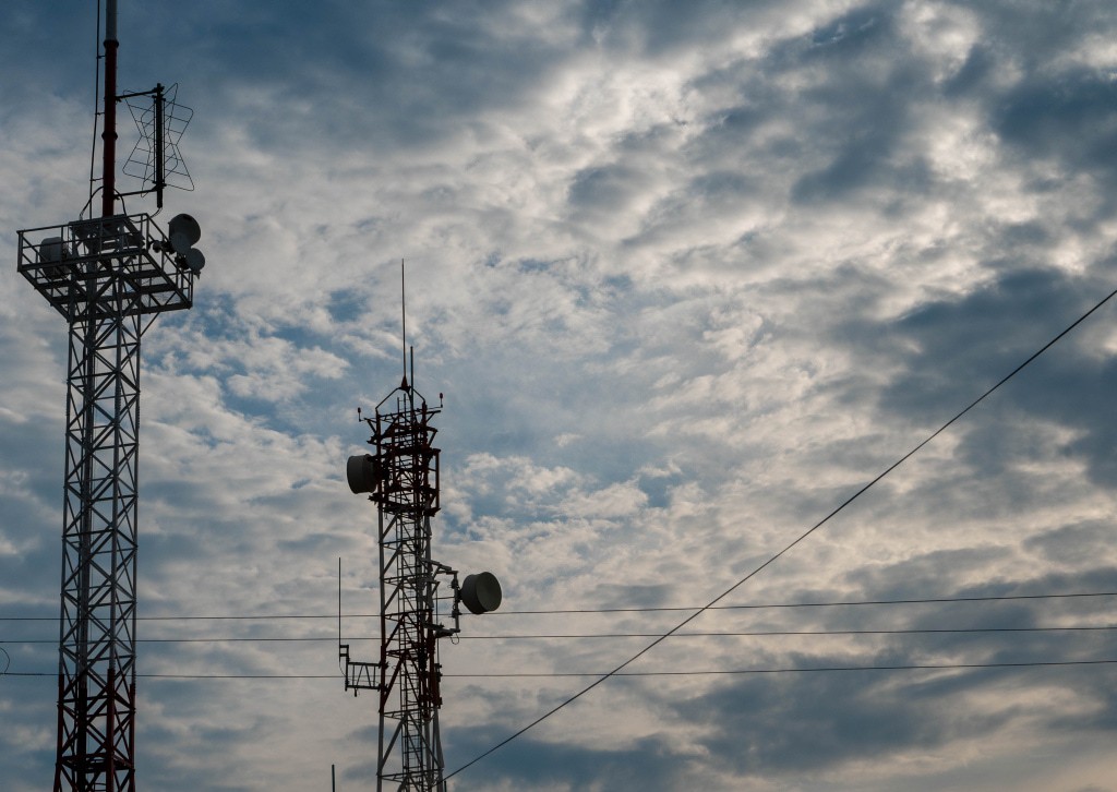 imagem colorida de duas torres de transmissão de energia elétrica com fundo de céu azul e nuvens brancas