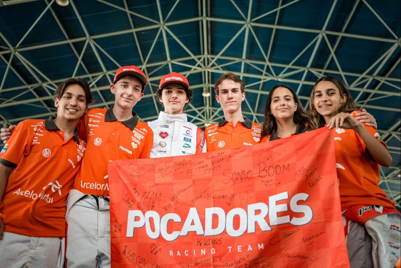 grupos de estudantes, de diferente raças, usam uniforme do time, que é laranja e branco, e seguram bandeira da equipe, com a escrita "Pocadores"