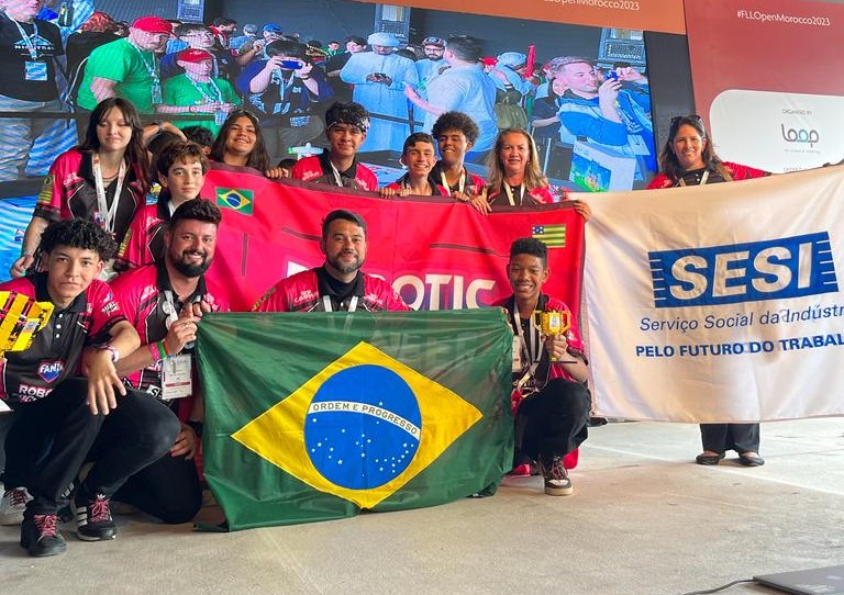 Alunos, que competiram no open internacional de robótica, estão segurando bandeira do Brasil, do SESI e  e da Equipe. Todos usam camiseta vermelha.