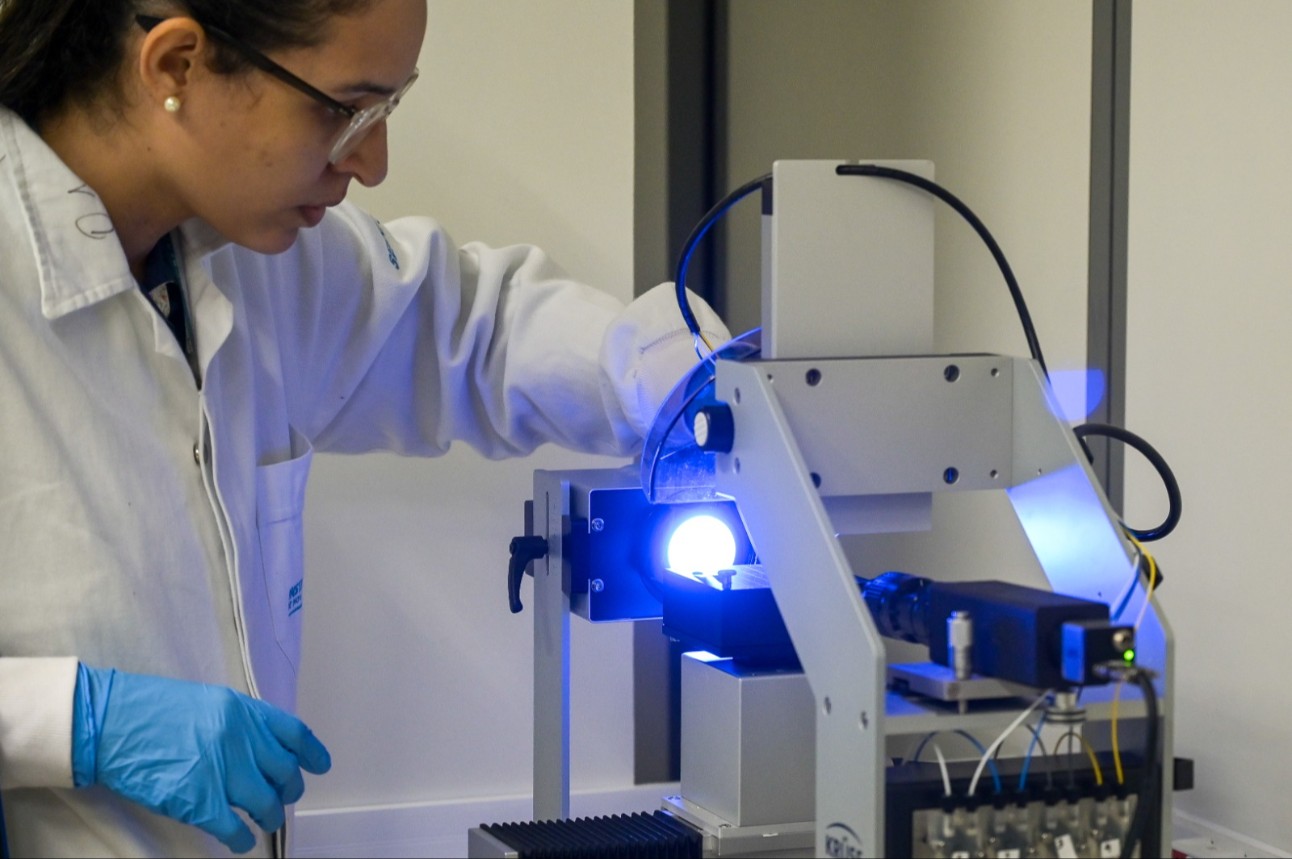 Pesquisadora opera equipamento de laboratório em ambiente científico.